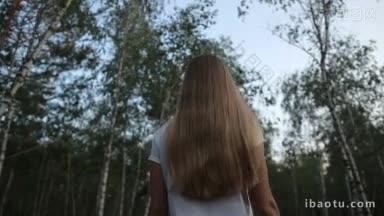 美丽的长金发女人走在桦树林在一个夏天的一天，在令人惊叹的景观背景背影